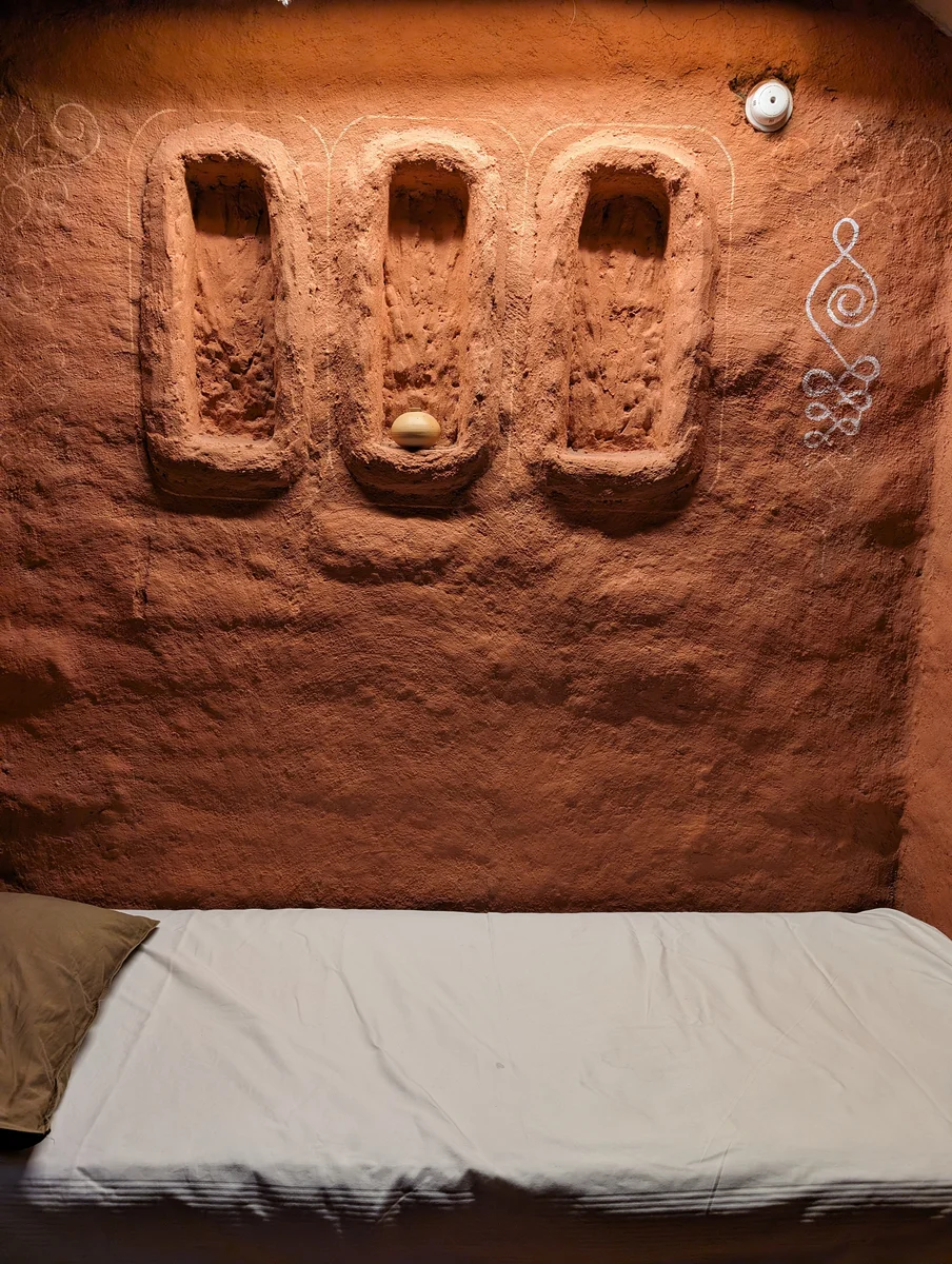 An earthen wall with recessed niches above a white bed