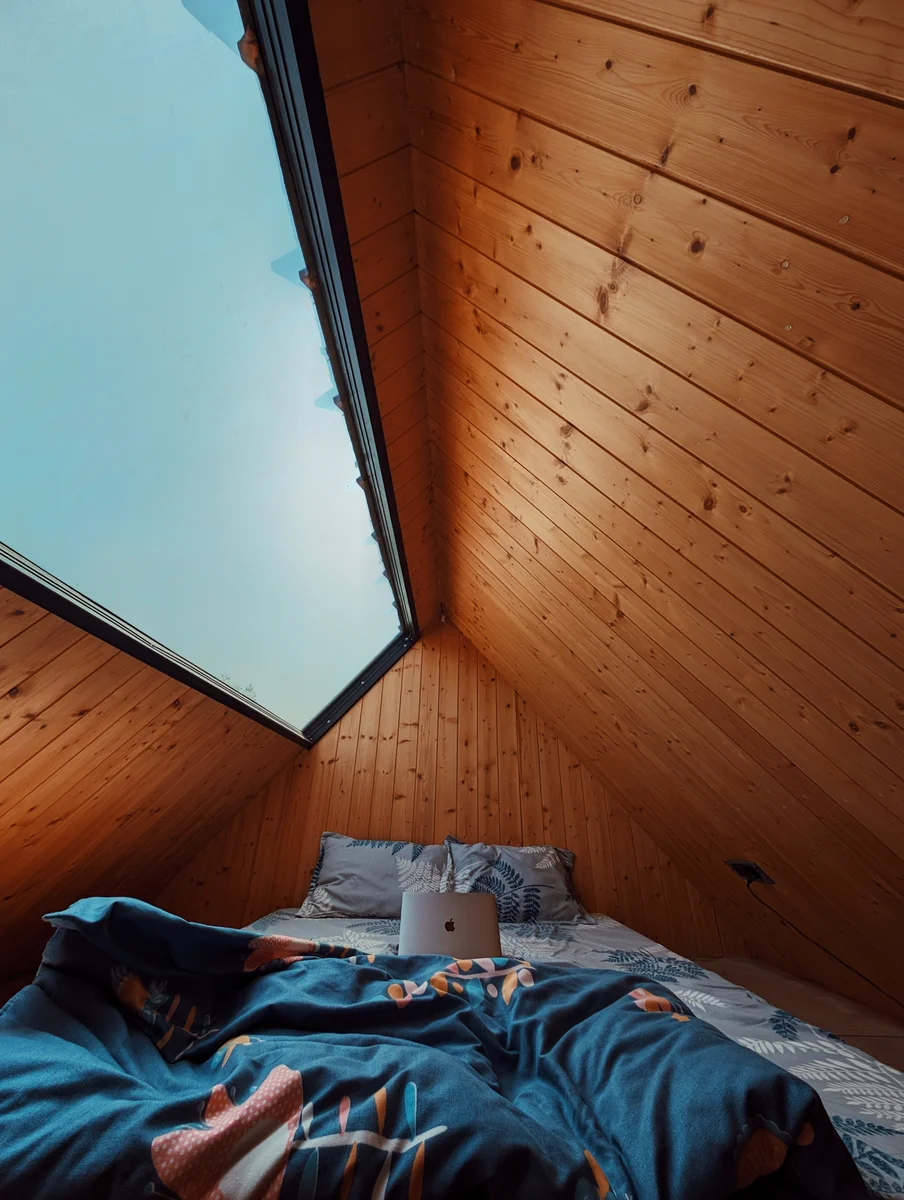 A bed beneath a timber roof and skylight